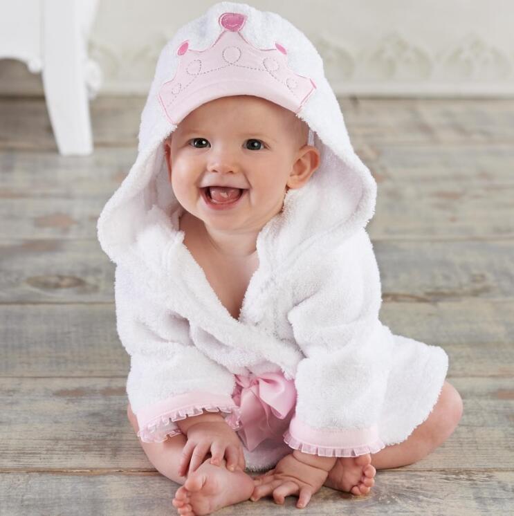 Baby wearing a soft white cotton hooded bathrobe with a pink crown applique, ruffled trim, and a matching pink sash.