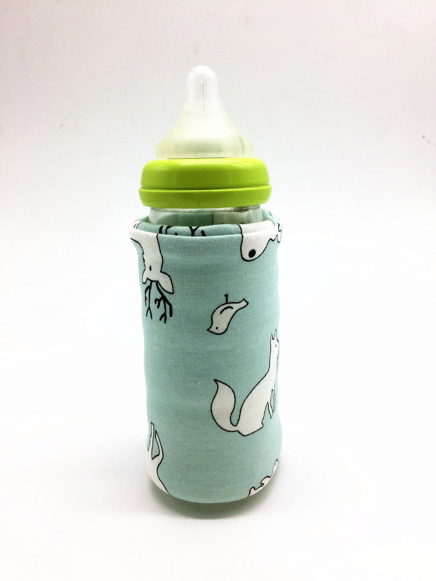 A baby bottle with a green cap inside a light blue fabric sleeve featuring a white woodland animal print.