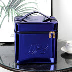 Shiny royal blue metallic makeup case with a top handle, zippered closure, and embossed logo on a glass table.