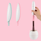 Hand holding a white electric makeup brush cleaner with pink or mint accents, shown with a brush inside a white bowl.