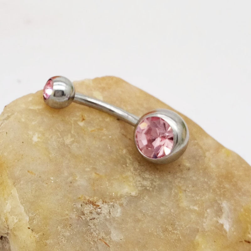 Hypoallergenic titanium steel belly button ring with a large pink crystal on a curved barbell, resting on a stone.