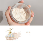 A hand holds a container of beige Maco Andy oil-control finishing powder, featuring a gold ballerina lid design.