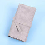 A grey faux leather roll-up makeup brush case with a tie closure, isolated against a light blue background.