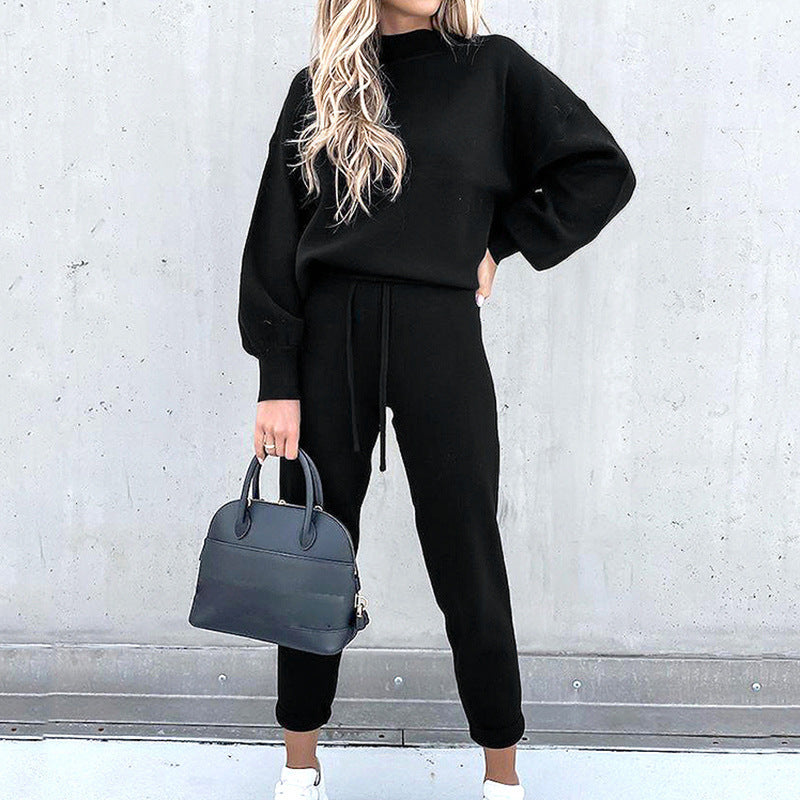 A woman wearing a black long-sleeve fleece sweater suit with a high neck, drawstring joggers, and a matching handbag.