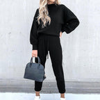 A woman wearing a black long-sleeve fleece sweater suit with a high neck, drawstring joggers, and a matching handbag.
