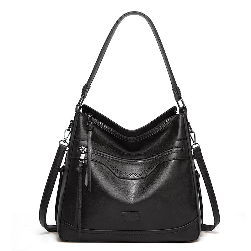Black vintage-style one-shoulder tote in soft leather with multiple zippered compartments and a long shoulder strap.