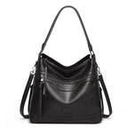 Black vintage-style one-shoulder tote in soft leather with multiple zippered compartments and a long shoulder strap.