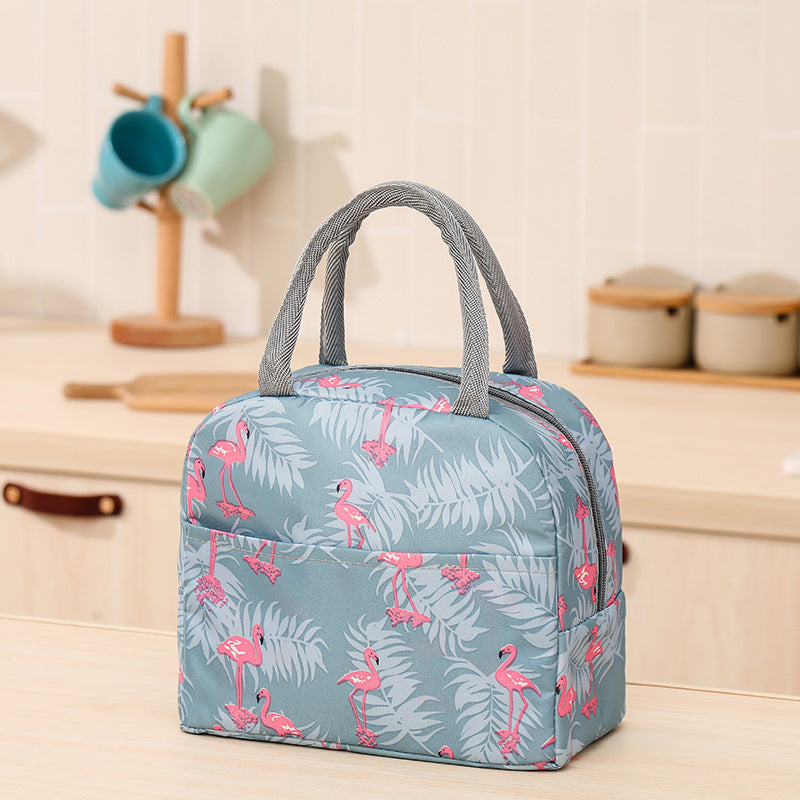 Blue cationic lunch bag with pink flamingo and leaf print, gray fabric handles, and zipper closure on a kitchen counter.
