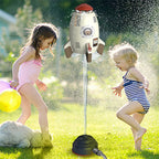 Two children play in a yard with a white and red plastic rocket sprinkler spraying water into the air.