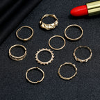A set of eight gold-tone metal hip hop rings featuring varied textured and minimalist designs on a black background.