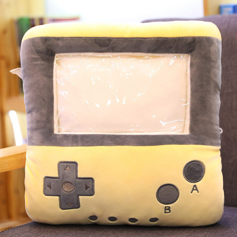 Yellow plush hand warmer pillow shaped like a vintage handheld game console with a clear vinyl screen pouch.