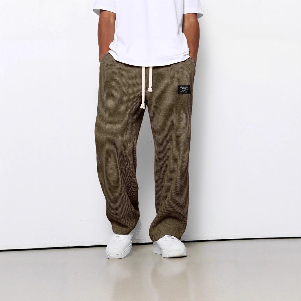 Loose-fit olive waffle-knit trousers with a cream drawstring, side pockets, and a small black brand patch.