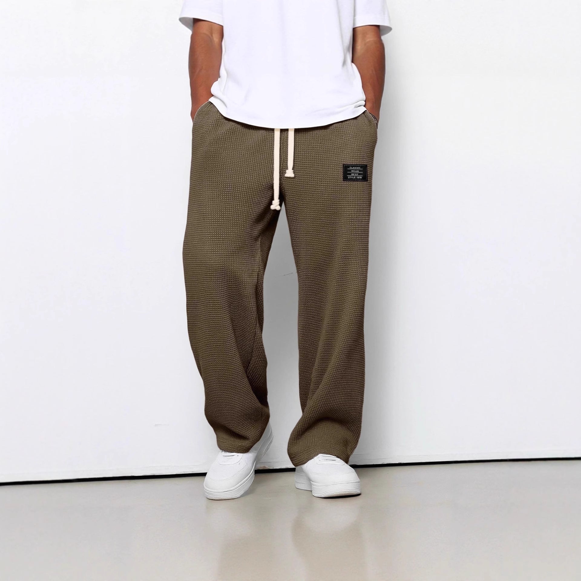 Loose-fit olive waffle-knit trousers with a cream drawstring, side pockets, and a small black brand patch.