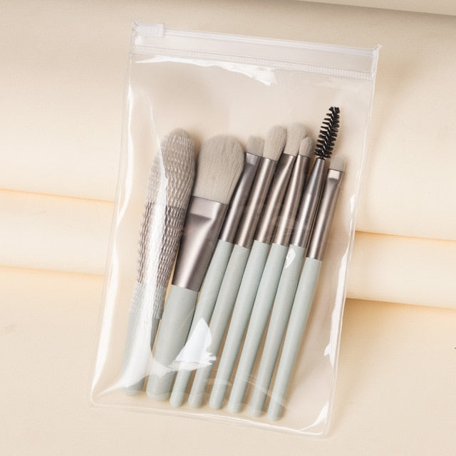 Eight-piece mini makeup brush set with sage green handles in a clear, zippered travel pouch.
