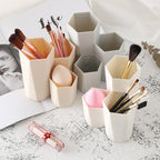 Beige and gray hexagonal makeup brush holders in various heights made of plastic, holding brushes and makeup sponges.