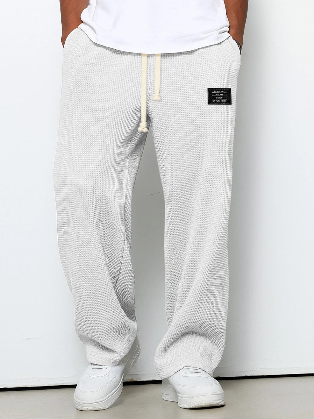 White waffle-knit loose-fit men’s pants with a drawstring waistband and small black rectangular patch detail.