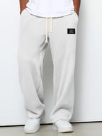 White waffle-knit loose-fit men’s pants with a drawstring waistband and small black rectangular patch detail.