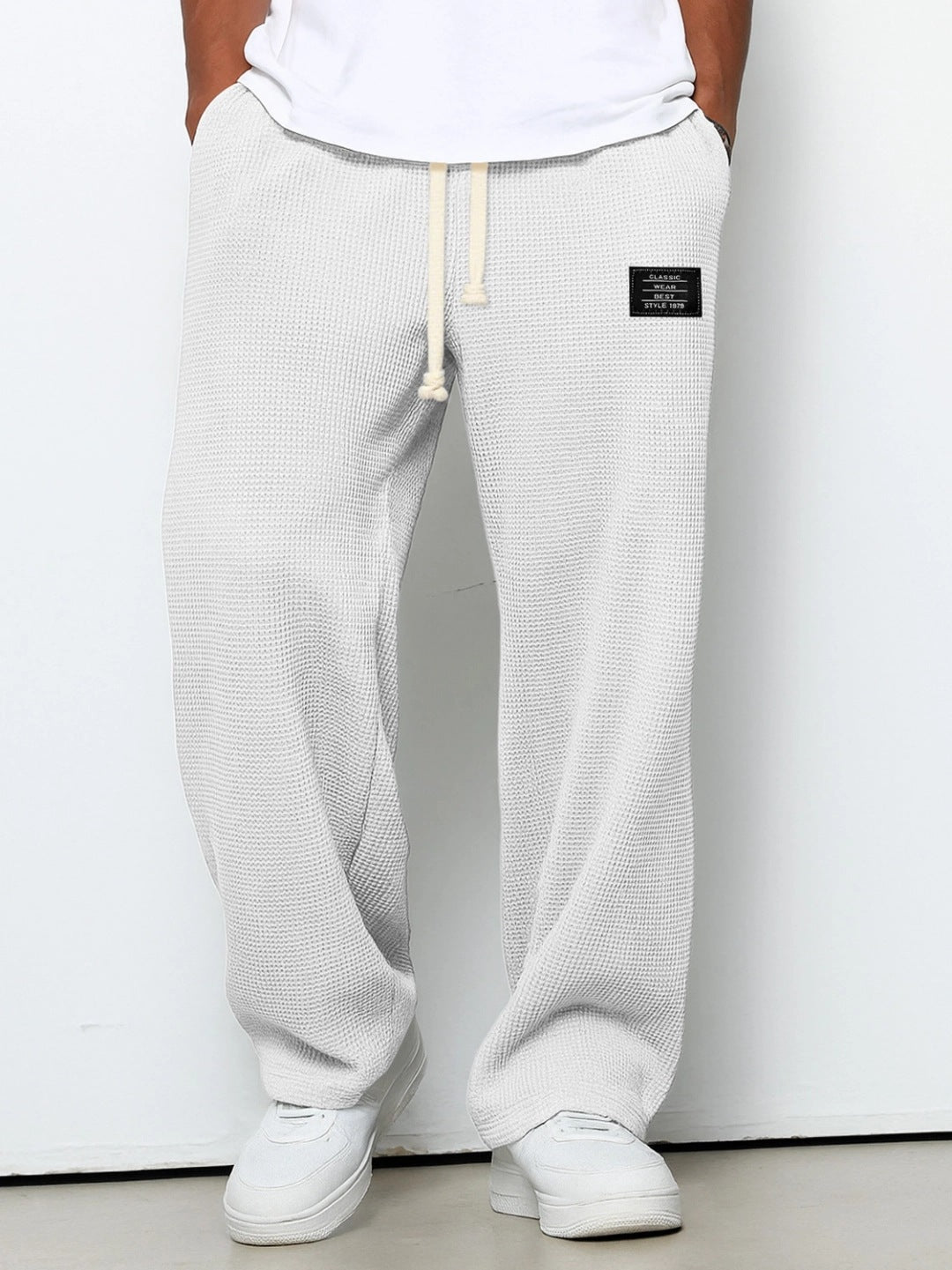 White waffle-knit loose-fit men’s pants with a drawstring waistband and small black rectangular patch detail.