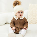Baby wearing a brown ribbed knit sweater bodysuit, white collared shirt, and a white pom-pom beanie.