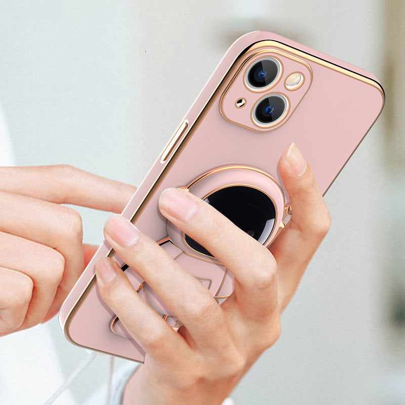 Pink phone case with gold electroplated trim and a 3D astronaut figure acting as a kickstand held in a person's hand.