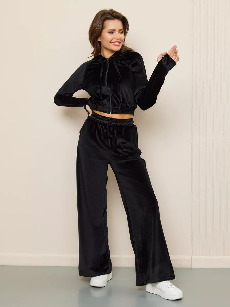 A woman wears a black velvet two-piece set featuring a cropped zip-up hoodie and matching wide-leg trousers.