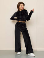 A woman wears a black velvet two-piece set featuring a cropped zip-up hoodie and matching wide-leg trousers.