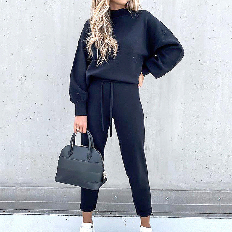 Woman wearing a black long-sleeve fleece sweater and matching drawstring pants, holding a black handbag.