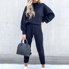 Woman wearing a black long-sleeve fleece sweater and matching drawstring pants, holding a black handbag.