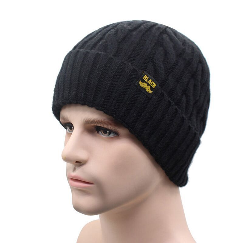 A black knitted beanie with a ribbed cuff and cable-knit pattern, featuring a small "BLACK" logo tab on the side.