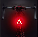 Bright red triangular LED bicycle taillight mounted under a black bike seat against a dark background.