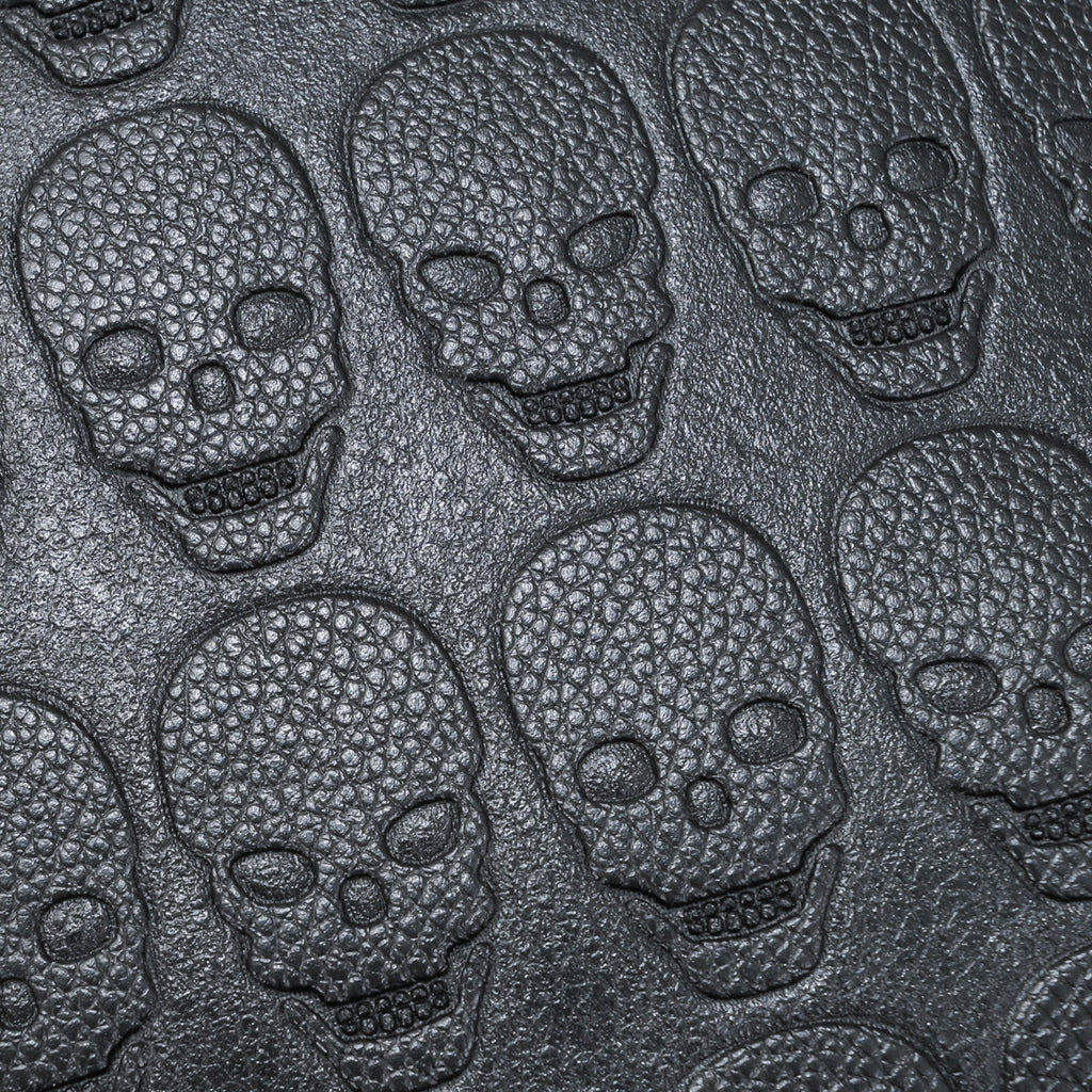 Close-up of black, textured soft leather embossed with a repeating skull pattern for a stylish, edgy backpack design.