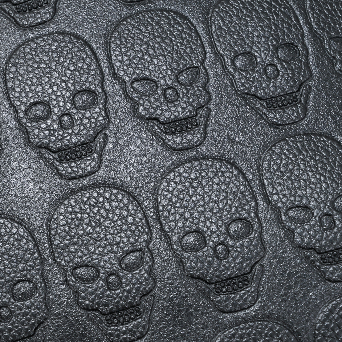 Close-up of black, textured soft leather embossed with a repeating skull pattern for a stylish, edgy backpack design.