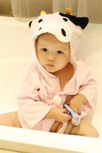 Baby in a light pink hooded cotton bathrobe featuring a cute cow face with black spots and yellow horns.