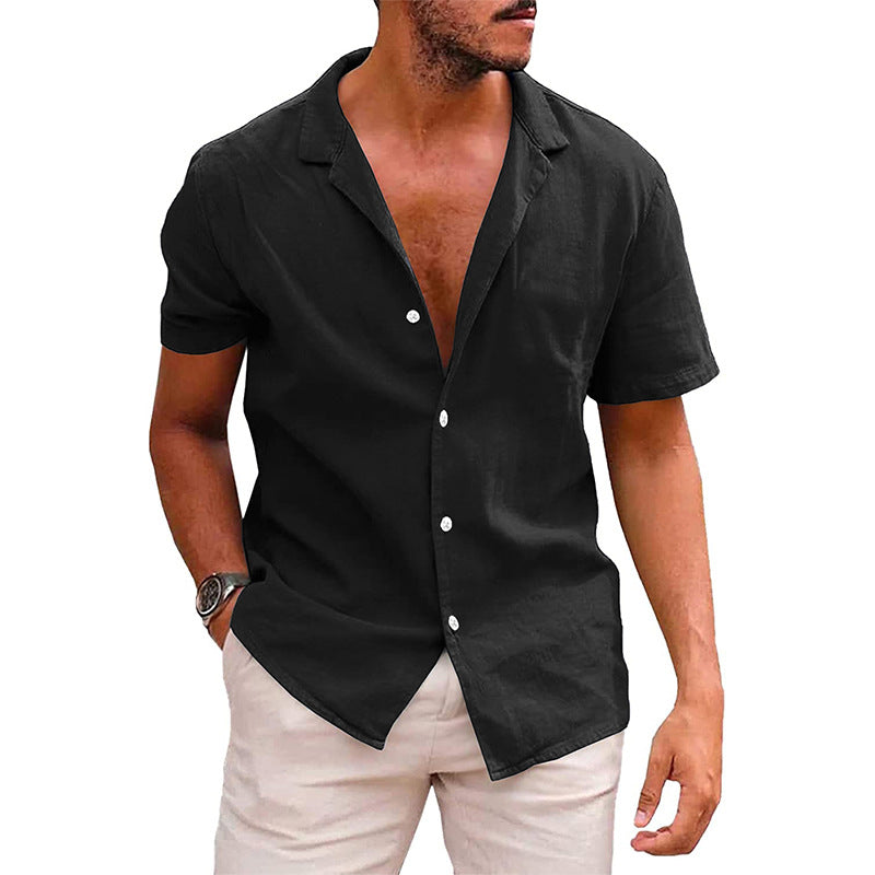 A man wears a short-sleeve, black button-down linen shirt with a relaxed camp collar, paired with light-colored pants.