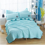 Light blue summer cooling quilt and two matching pillowcases with black trim on a bed in a bright bedroom.