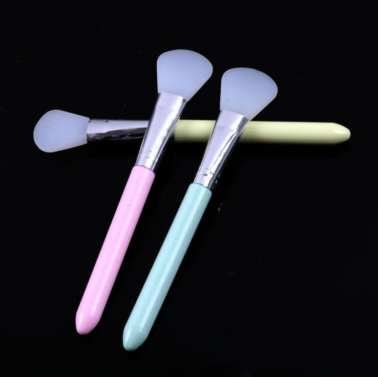 Three silicone face mask brushes with silver ferrules and pastel pink, mint, and yellow handles on a black background.
