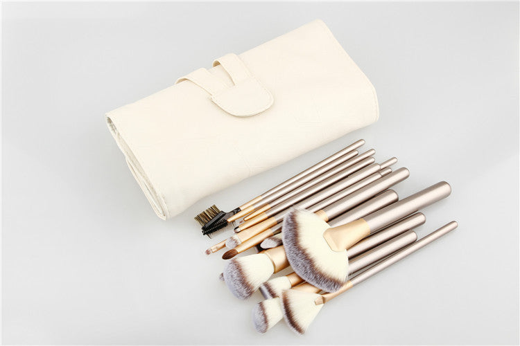 A 24-piece makeup brush set with metallic champagne handles and soft white bristles, including a white roll-up case.