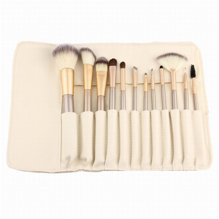 A set of makeup brushes with white bristles and gold ferrules, arranged in a cream-colored roll-up case.