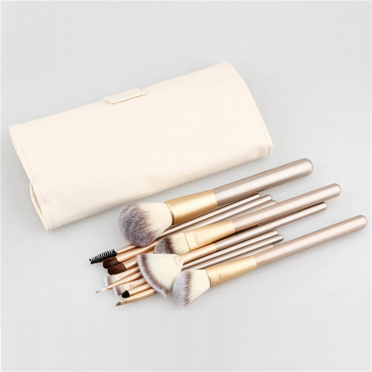 A set of 24 makeup brushes with champagne gold handles and a cream-colored leather carrying case on a white background.