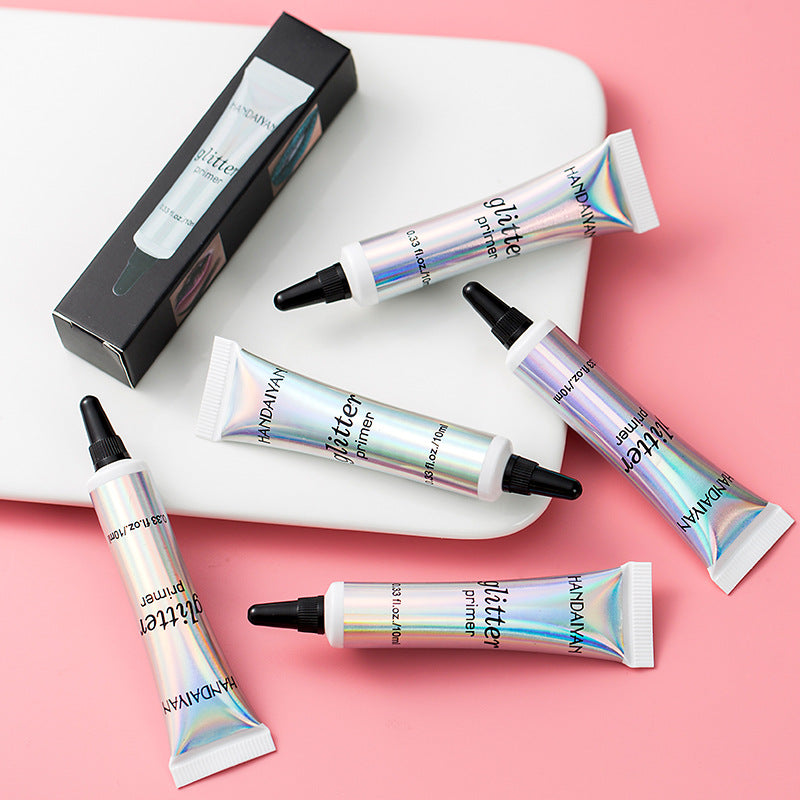 Five iridescent Handaiyan glitter primer squeeze tubes and one black box on a white tray against a pink background.