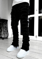 Men's black stacked jeans with heavy distressed fringe detailing, tight fit, and raw hems worn with white sneakers.