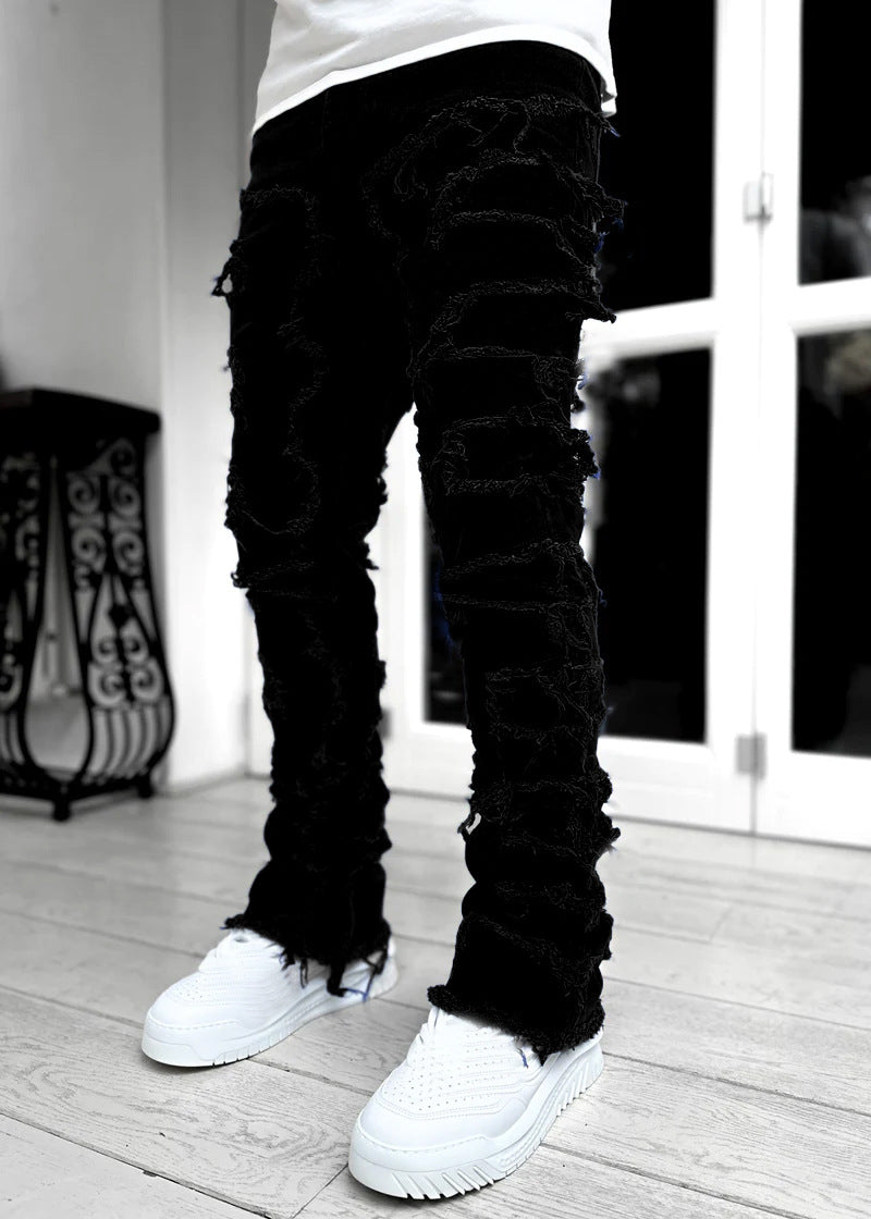 Men's black stacked jeans with heavy distressed fringe detailing, tight fit, and raw hems worn with white sneakers.