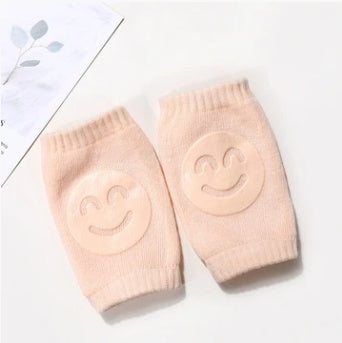 Pair of beige, ribbed terry cloth baby knee pads featuring non-slip, smiling face silicone patches for crawling.