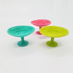 Three silicone makeup brush cleaning pads in teal, pink, and lime green, each with a suction cup base and textures.