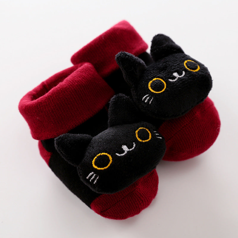 Soft red and black baby socks featuring plush 3D black cat faces with yellow embroidered eyes and whiskers.