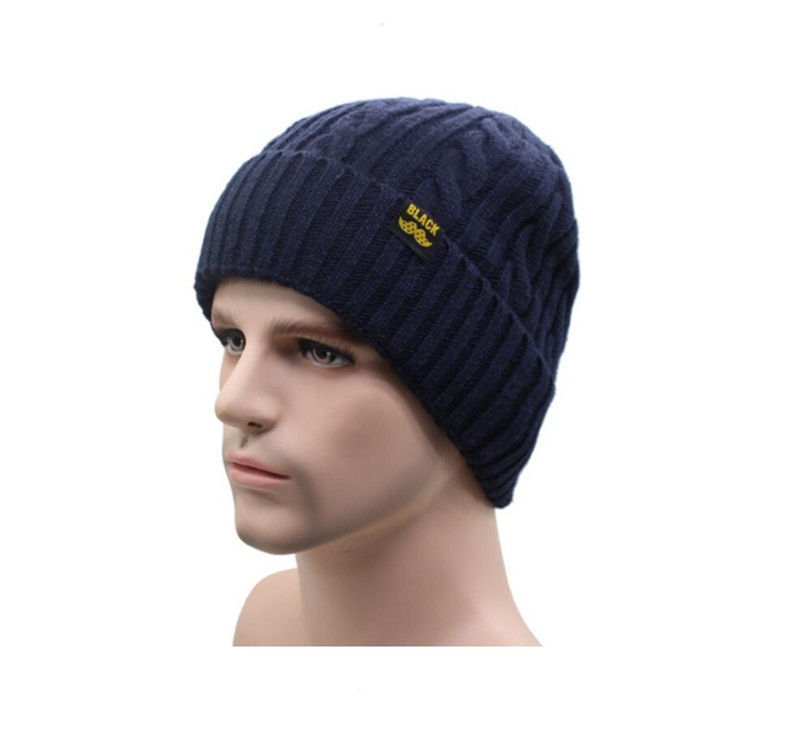 A man wearing a navy blue cable-knit beanie with a ribbed cuff and a small "BLACK" patch on the front.