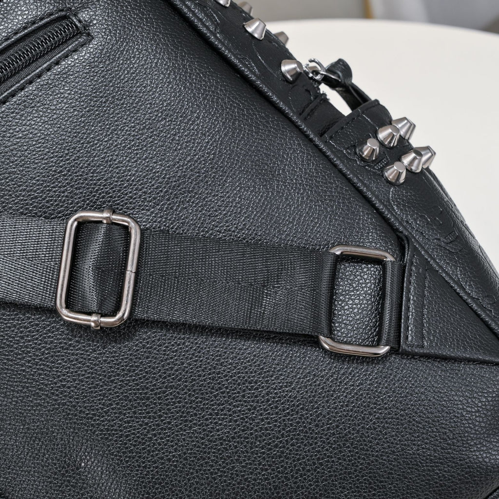 Black pebble-grain leather backpack with silver metal studs, adjustable fabric strap, and metal buckles.