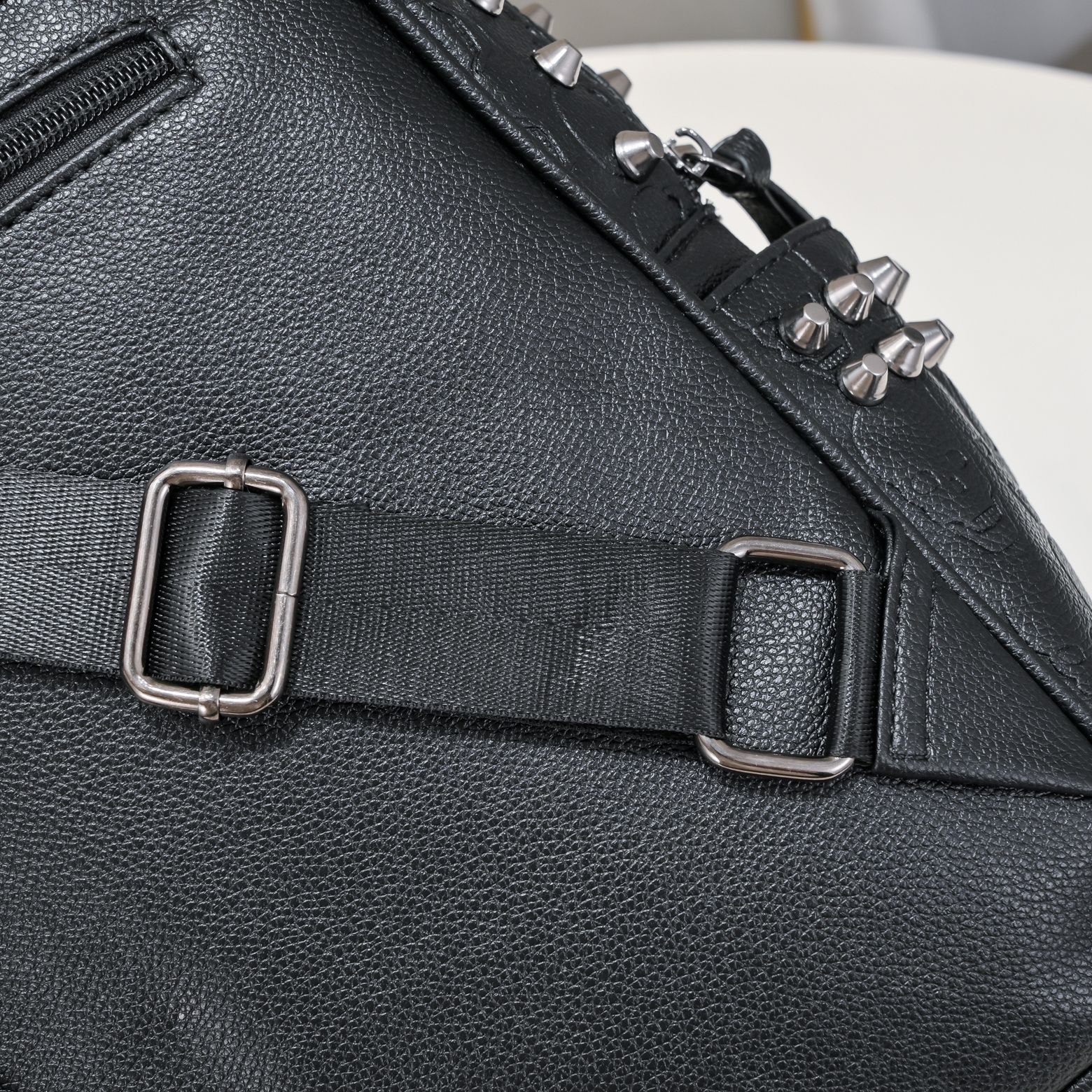 Black pebble-grain leather backpack with silver metal studs, adjustable fabric strap, and metal buckles.