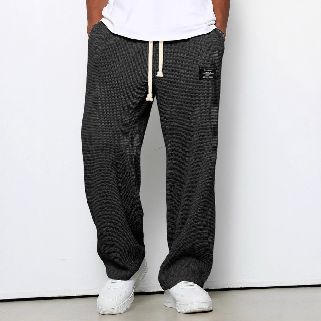 Charcoal grey men's waffle-knit straight-leg trousers with a white drawstring waist and a small rectangular logo patch.