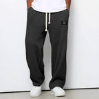 Charcoal grey men's waffle-knit straight-leg trousers with a white drawstring waist and a small rectangular logo patch.